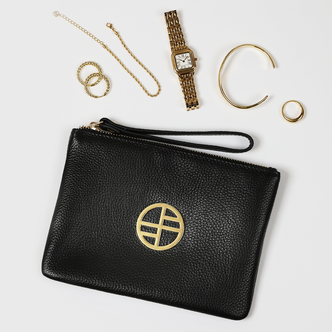 Black leather pouch bag with gold details on white background, gold jewellery and watch on white background