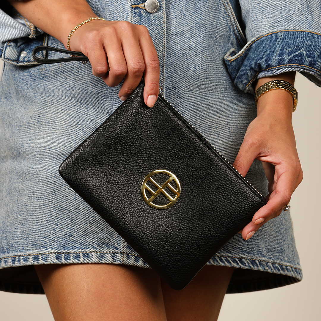 Woman wearing denim dress, holding black leather pouch bag with gold details