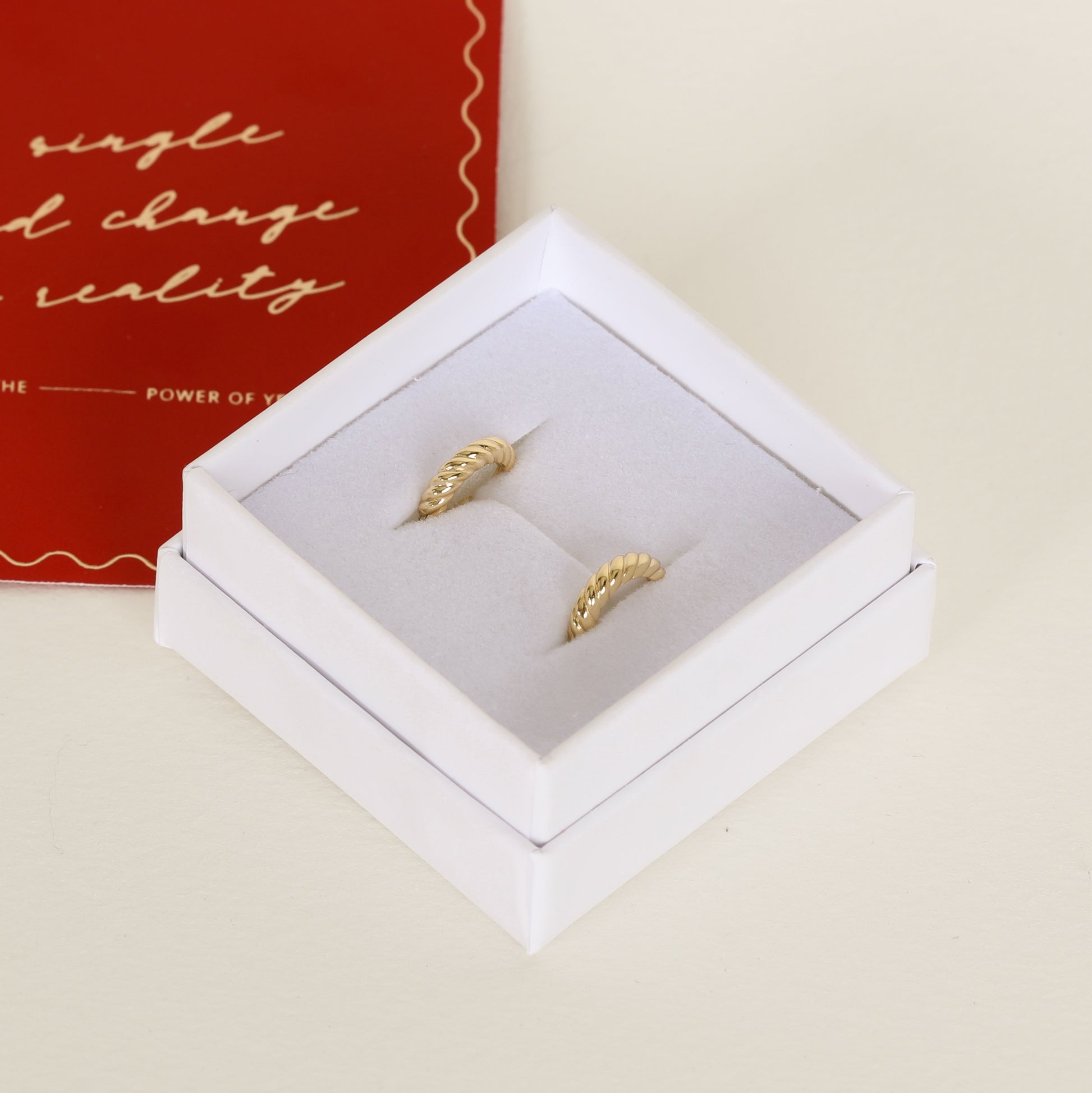 gold delicate huggies with a twist design on white box 