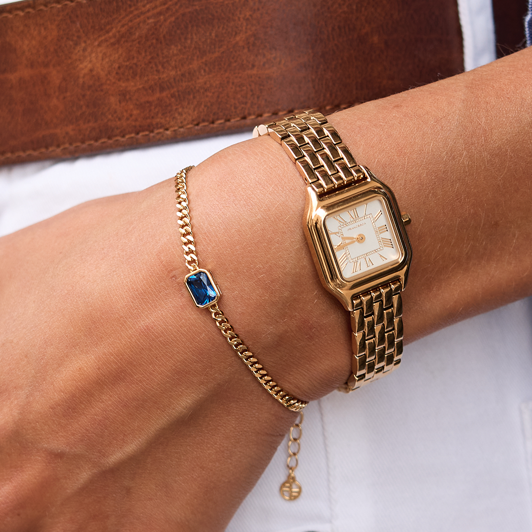 Gold chain bracelet with Navy blue cubic zirconia bezel set in centre Inspired by the halls of Versailles on wrist next to gold watch 
