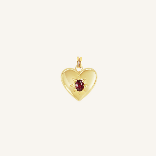 gold heart shaped charm with deep red oval cubic zirconia on white background
