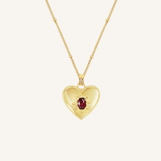 gold heart shaped charm with deep red oval cubic zirconia on bobble chain on white background
