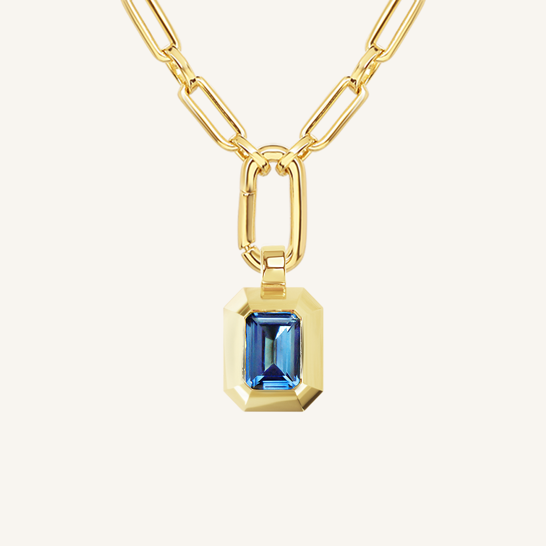 Gold charm with Blue emerald cut cubic zirconia bezel set Inspired by the halls of Versailles on link chain on white background 