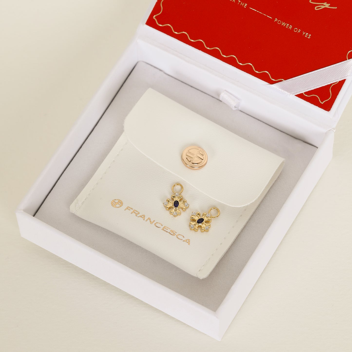 gold hoop charms that features the intricate fleur-de-lis details found in the iconic Palace of Versailles accompanied by the deep blue stone on white box