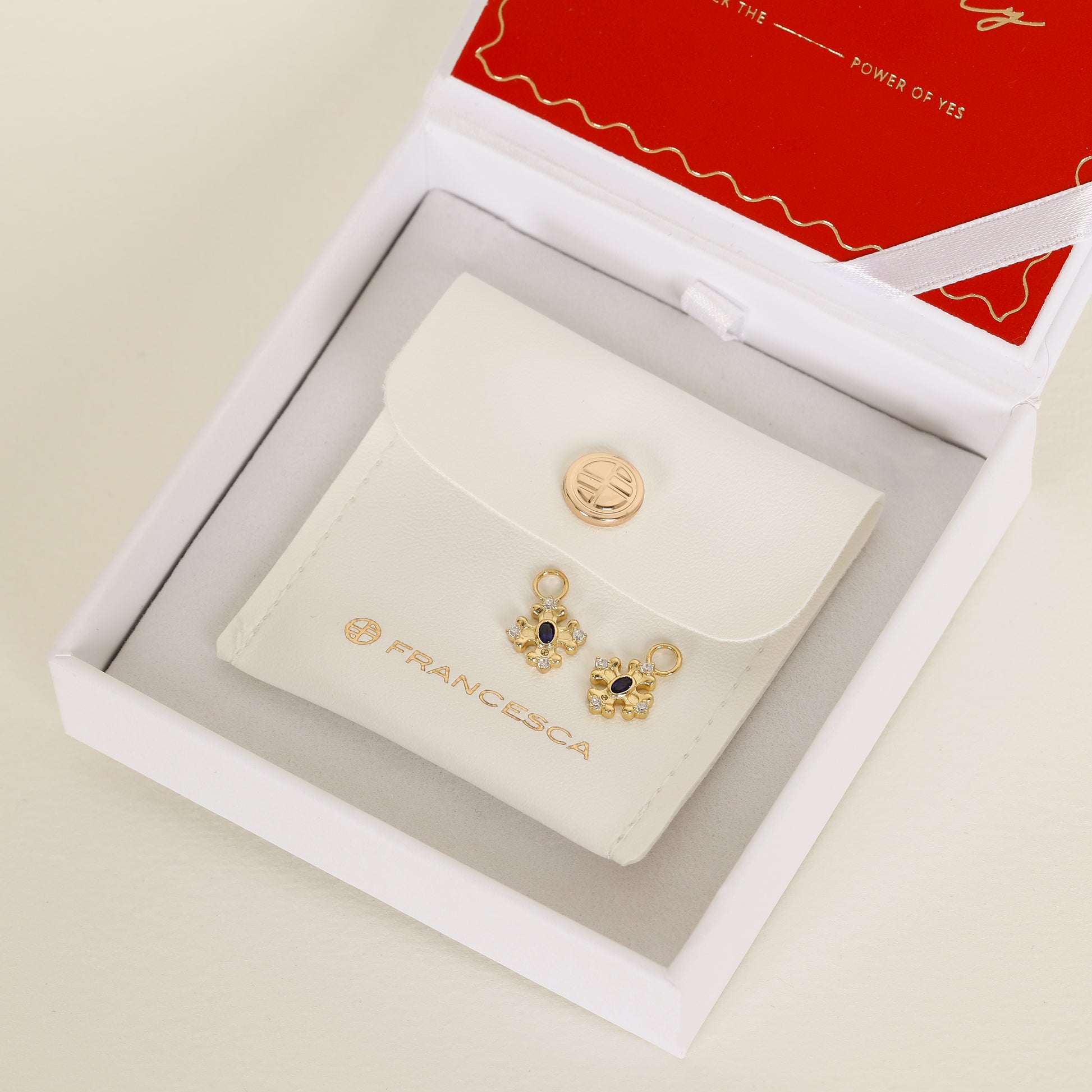 gold hoop charms that features the intricate fleur-de-lis details found in the iconic Palace of Versailles accompanied by the deep blue stone on white box