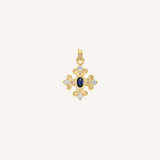 gold charm that features the intricate fleur-de-lis details found in the iconic Palace of Versailles accompanied by the deep blue stone on white background
