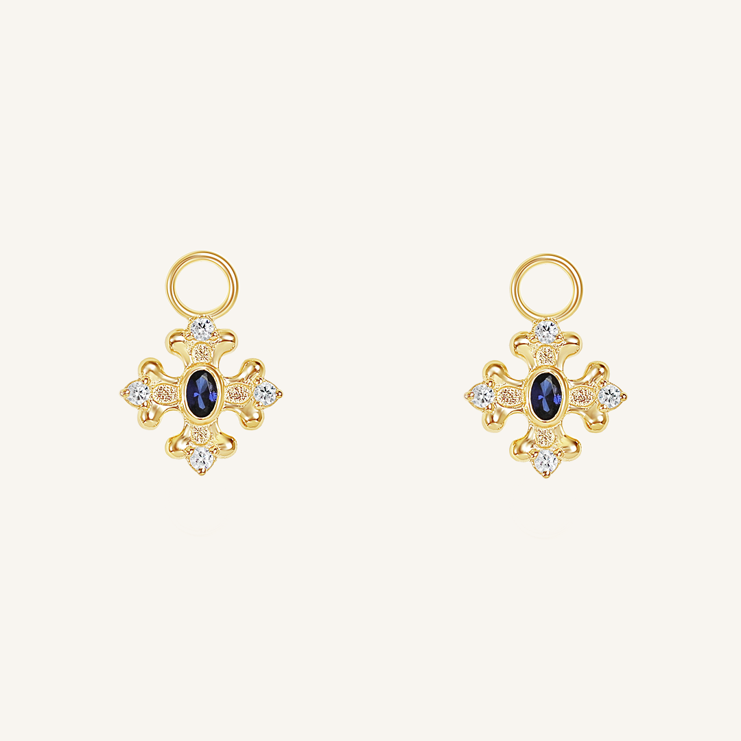 gold hoop charms that features the intricate fleur-de-lis details found in the iconic Palace of Versailles accompanied by the deep blue stone on white background