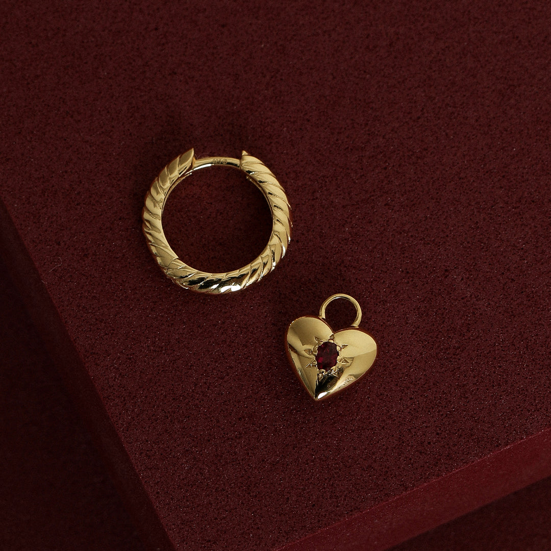 gold hoop charm with heart charms with deep red oval cubic zirconias next to gold hoop on red background